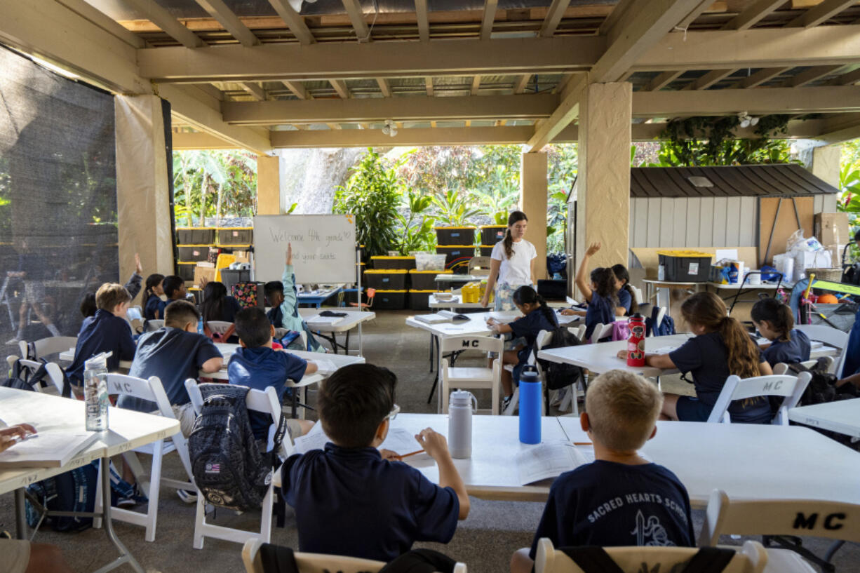 Sacred Hearts School second grade teacher Courtney Copriviza interacts with the fourth graders at their temporary school site at Sacred Hearts Mission Church on Tuesday, Oct. 3, 2023, in Lahaina, Hawaii. Sacred Hearts and other private schools across the state took in displaced public school students and offered a year of free tuition. The three public schools that survived the deadly August wildfire are set to reopen this week.