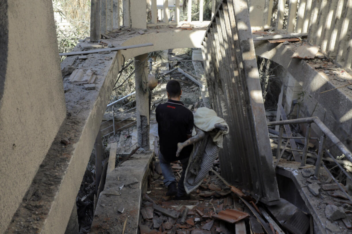 A Palestinian man carries a body found inside a destroyed house following Israeli airstrikes on Gaza City, Thursday, Oct.19, 2023.