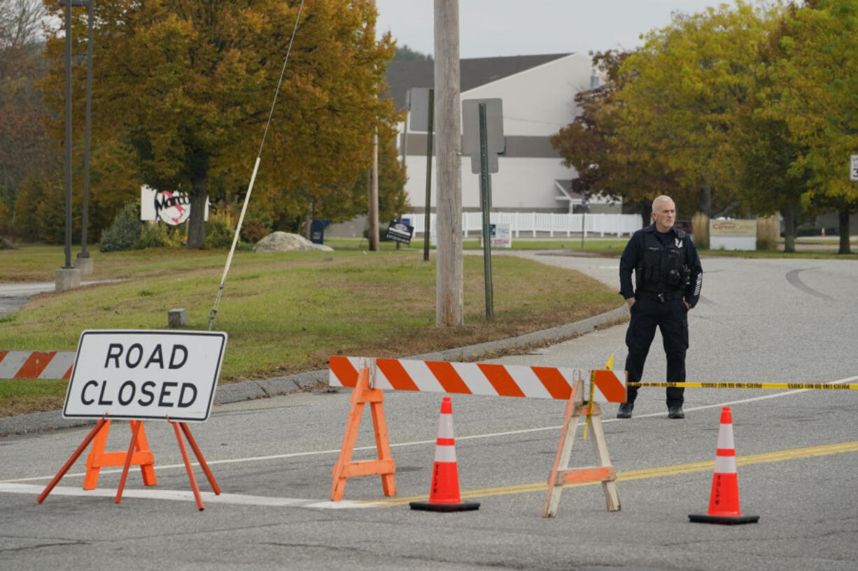 A police officer stands at a road closure near a bowling alley, seen in background, Thursday, Oct. 26, 2023, in Lewiston, Maine. The site is one of Wednesday's two mass shootings in the city. Residents have been ordered to shelter in place as police continue to search for the suspect. (AP Photo/Robert F.