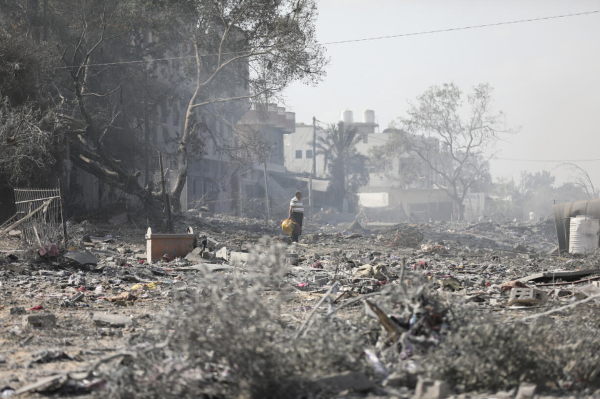 Palestinians walk by the buildings destroyed in the Israeli bombardment on al-Zahra, on the outskirts of Gaza City, Friday, Oct. 20, 2023.