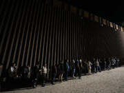 FILE - People line up against a border wall as they wait to apply for asylum after crossing the border from Mexico. Tuesday, July 11, 2023, near Yuma, Ariz. As the number of migrants coming to the U.S.'s southern border is climbing, the Biden administration aims to admit more refugees from Latin America and the Caribbean over the next year. The White House Friday, Sept. 29, released the targets for how many refugees it aims to admit over the next fiscal year starting October 1 and from what regions of the world.