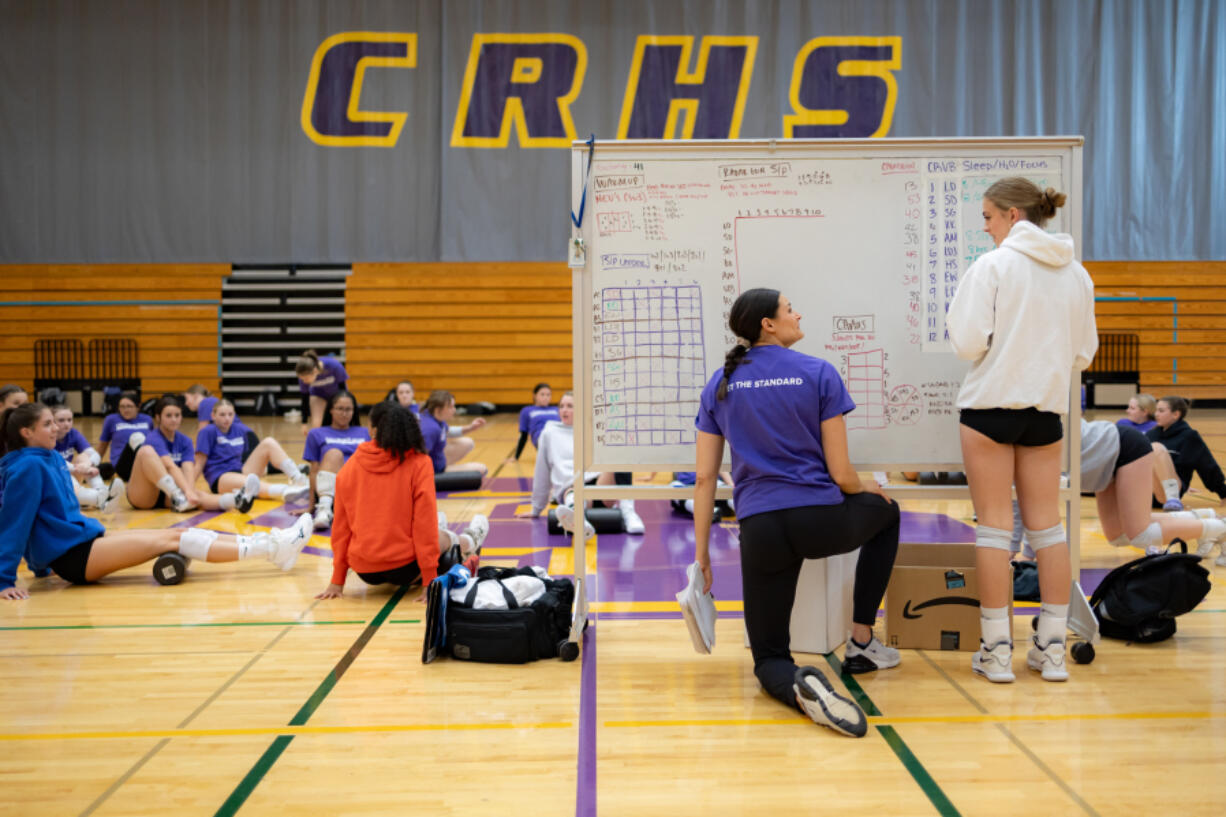 Columbia River High volleyball coach Breanne Smedley talks to senior Evie Wenger while the rest of the team warms up before their practice Oct. 18 inside Columbia River High School&rsquo;s gym. River is the two-time defending Class 2A state champion ahead of the state volleyball state tournament this weekend in Yakima.