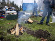 Smoke billows from a campfire under cold conditions as Vancouver resident Greg Wilson, background left, who is not a resident of the Burnt Bridge Creek encampment, helps his friend set up his gear in the new location Wednesday morning.