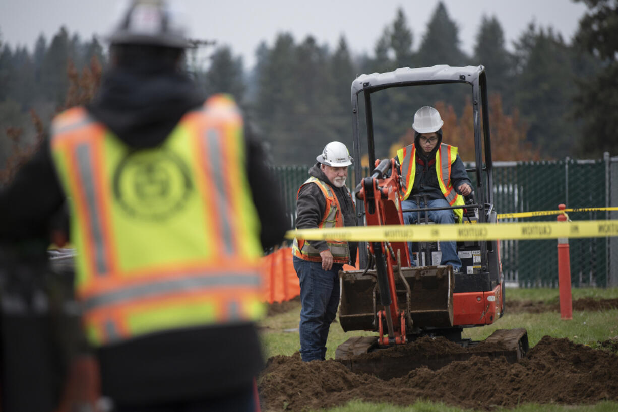 Tapani&rsquo;s John Jordan, left, looks on as Evergreen High School junior Isaiah Florendo, 16, gives a mini-excavator a try on Thursday morning.