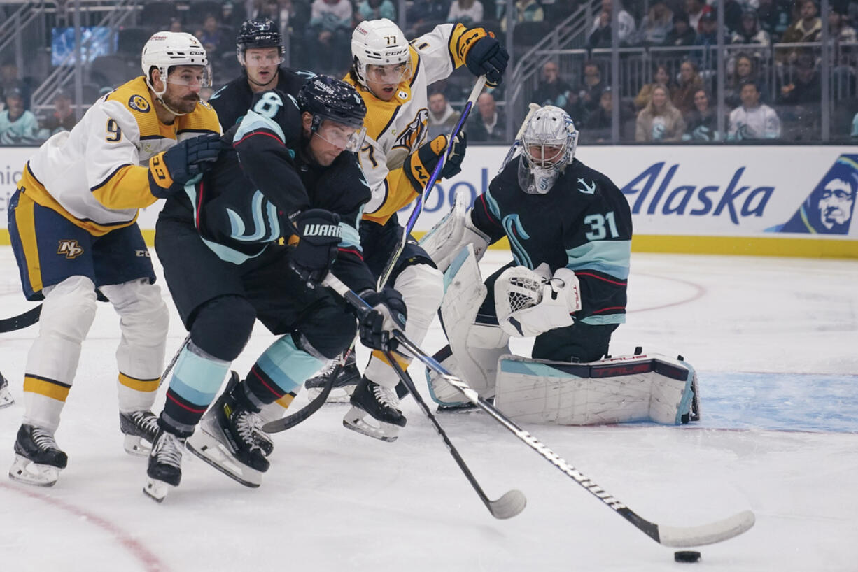 Seattle Kraken defenseman Brian Dumoulin (8) tries to keep the puck away from Nashville Predators left wing Filip Forsberg (9) and right wing Luke Evangelista (77) as Kraken goaltender Philipp Grubauer (31) watches during the first period of an NHL hockey game Thursday, Nov. 2, 2023, in Seattle.