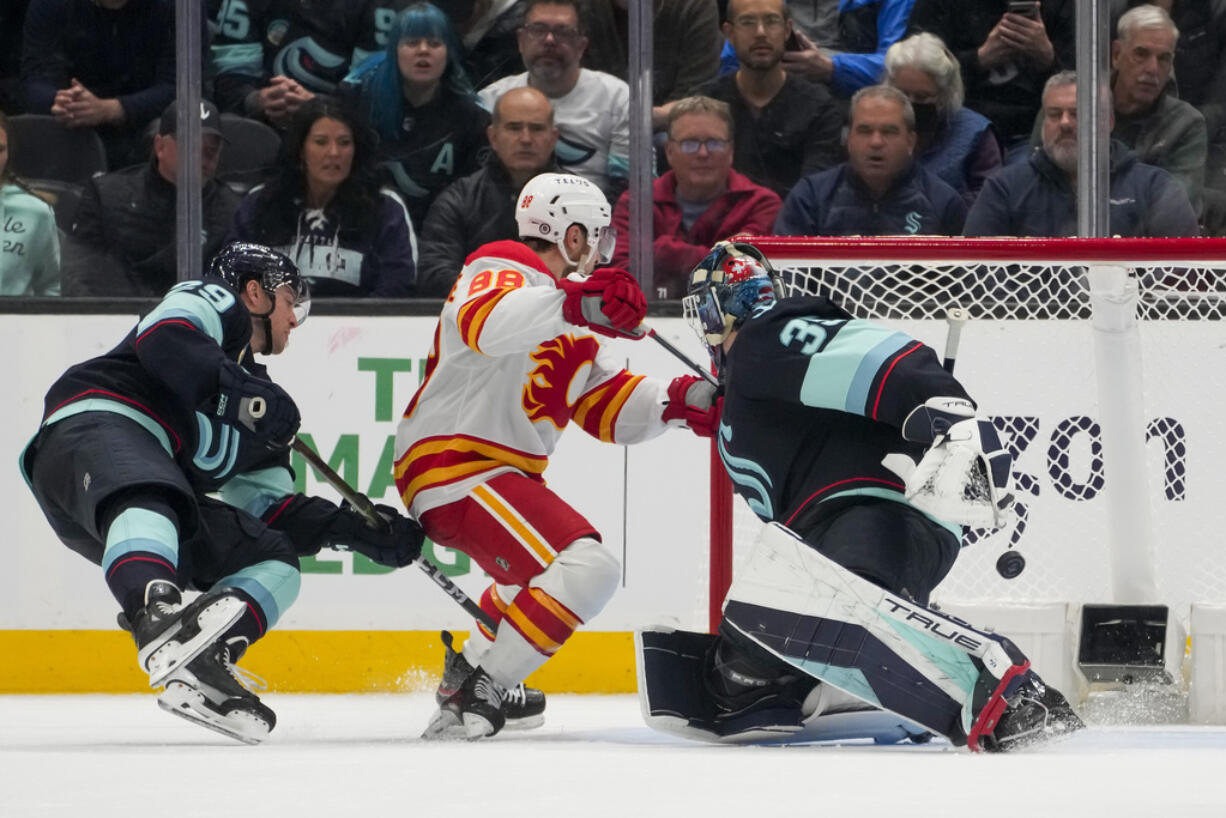 Calgary Flames left wing Andrew Mangiapane (88) scores behind Seattle Kraken goaltender Joey Daccord, right, as defenseman Vince Dunn, left, falls during the third period of an NHL hockey game Monday, Nov. 20, 2023, in Seattle. The Flames won 4-3 in overtime.