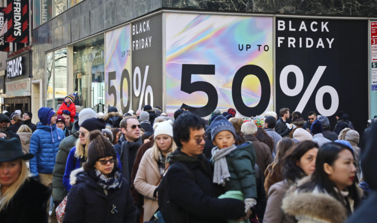 File - Crowds walk past a large store sign displaying a Black Friday discount in midtown Manhattan, Friday, Nov. 23, 2018, in New York. While Black Friday may no longer look like the crowd-filled, in-person mayhem that it was just decades ago &mdash; in large part due to the rising dependence on online shopping that was accelerated by the COVID-19 pandemic &mdash; the holiday sales event is still slated to attract millions of consumers.