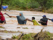 FILE - Residents cross a road damaged during flooding in Tula, Tana River county in Kenya on Nov. 25, 2023.