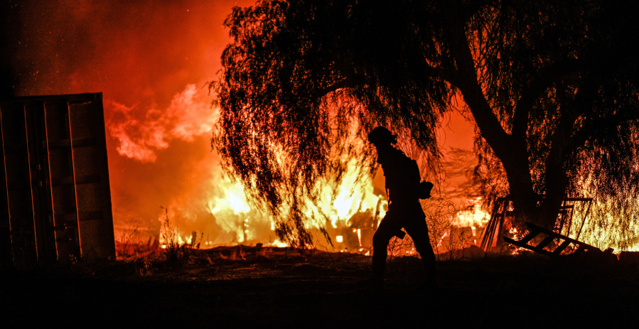 A photojournalist walks among the flames of a wildfire in rural Aguanga, Calif. Monday, Oct. 30, 2023.