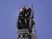 FILE - Visitors wearing masks ride on a roller coaster at Six Flags Magic Mountain on its first day of reopening to members and pass holders in Valencia, Calif., on April 1, 2021. Cedar Fair and Six Flags Entertainment Corp. are merging, creating an expansive amusement park operator with operations spread across 17 states and three countries. (AP Photo/Jae C.