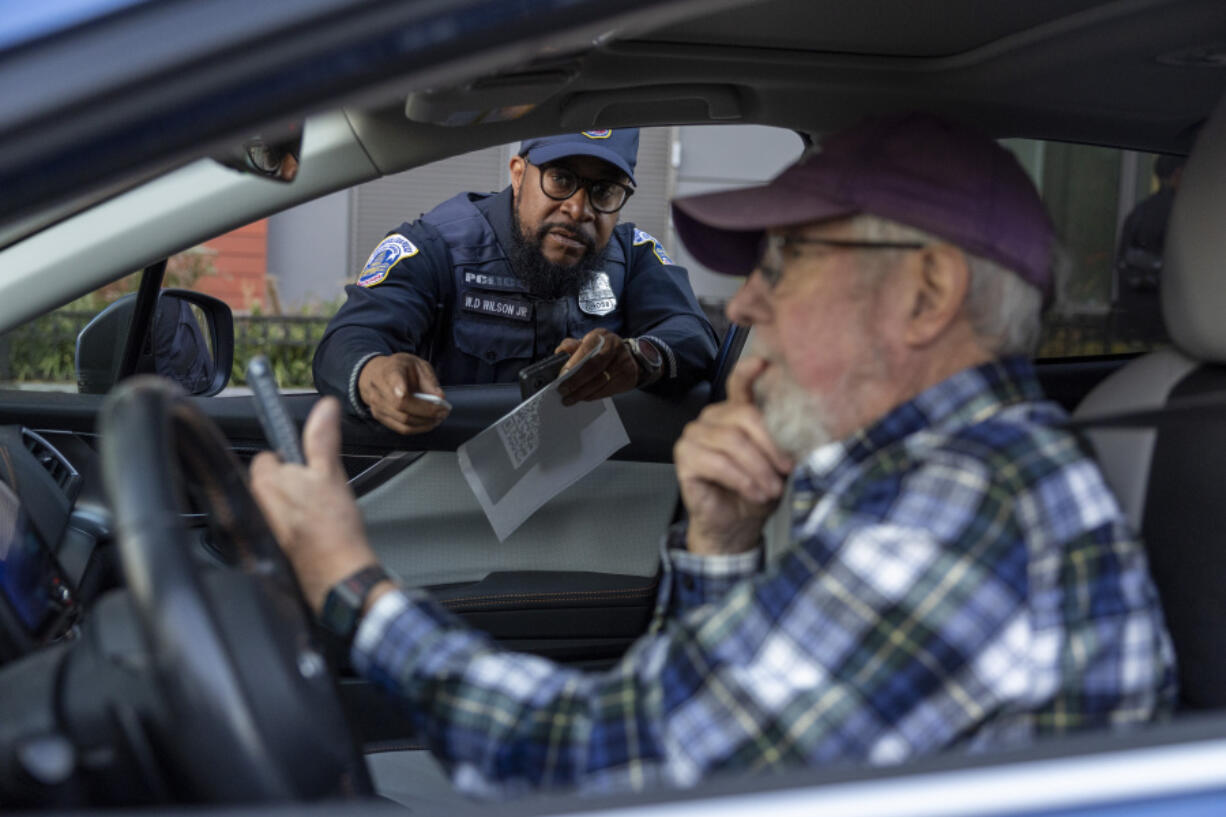 Metropolitan Police Department officer Muhammad Lewis explains to Nils Bruzelius how to use a Tile tracker during an event where police officers distributed mobile tracking devices for cars to drivers in an attempt to curb a rise in crime in Washington on Tuesday, Nov. 7, 2023.