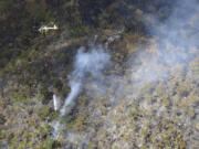 This photo provided by the Hawaii Department of Land and Natural Resources shows a helicopter dropping water on a wildfire burning east of Mililani, Hawaii, on Thursday, Nov. 2, 2023. A wildfire that has burned forestlands in a remote mountainous area of Central Oahu has moved eastward and away from population centers as firefighters continued to battle the blaze.