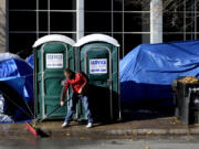 A migrant man sweeps the sidewalk of leaves and melting snow in a small tent community, Wednesday, Nov. 1, 2023, near a Northside police station in Chicago.