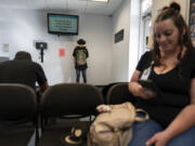 A person signs in, center, as Jesse Johnson of the Family Resource Center, right, waits for client Tyler Baker to complete a random drug test at the Hancock County Adult Probation office in Findlay, Ohio, Thursday, Oct. 12, 2023. Experts say establishing peer support programs to help people in recovery is one way communities should consider using money from settling lawsuits with the drug industry over the toll of opioids.