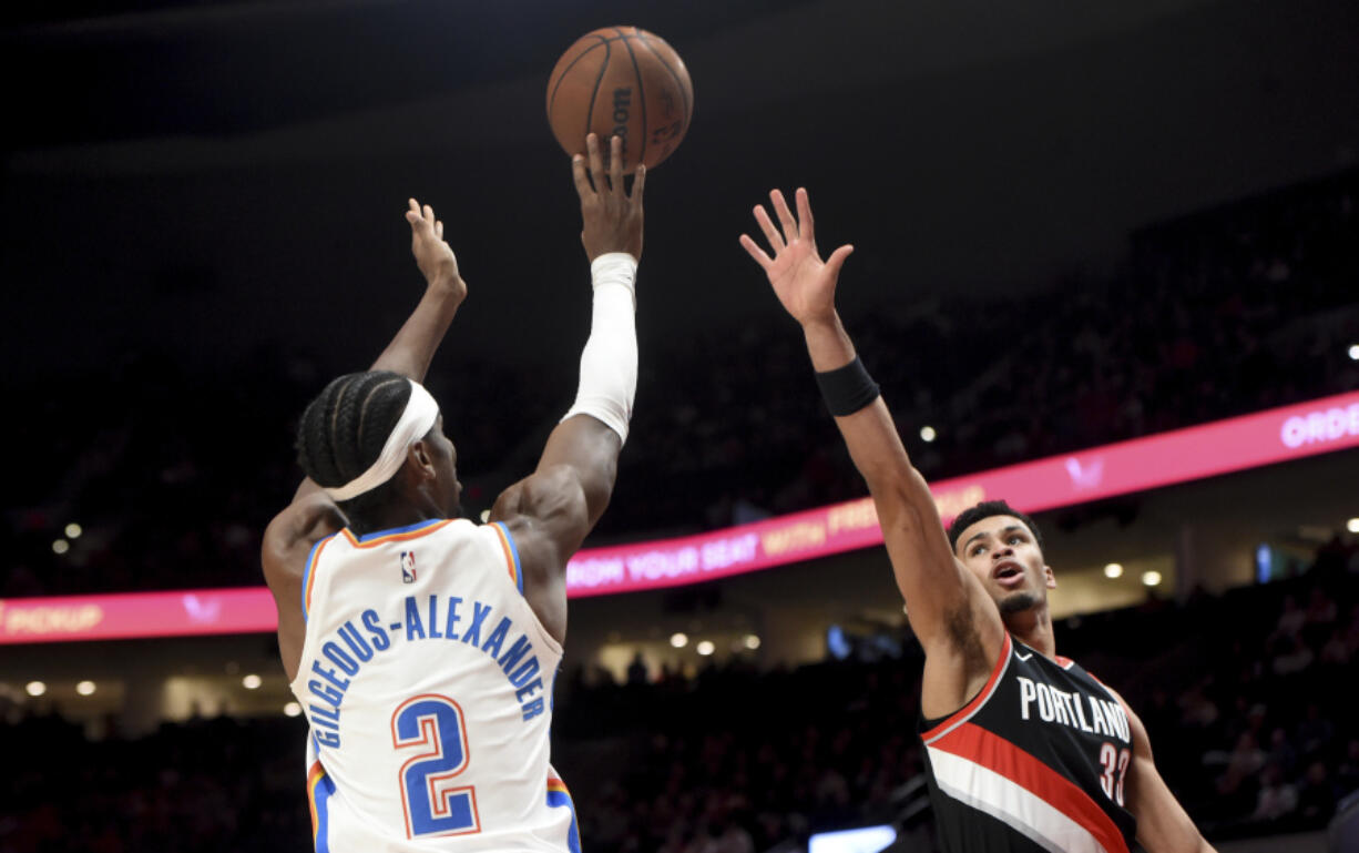 Oklahoma City Thunder guard Shai Gilgeous-Alexander, left, hits a shot over Portland Trail Blazers forward Toumani Camara, right, during the first half of an NBA basketball game in Portland, Ore., Sunday, Nov. 19, 2023.