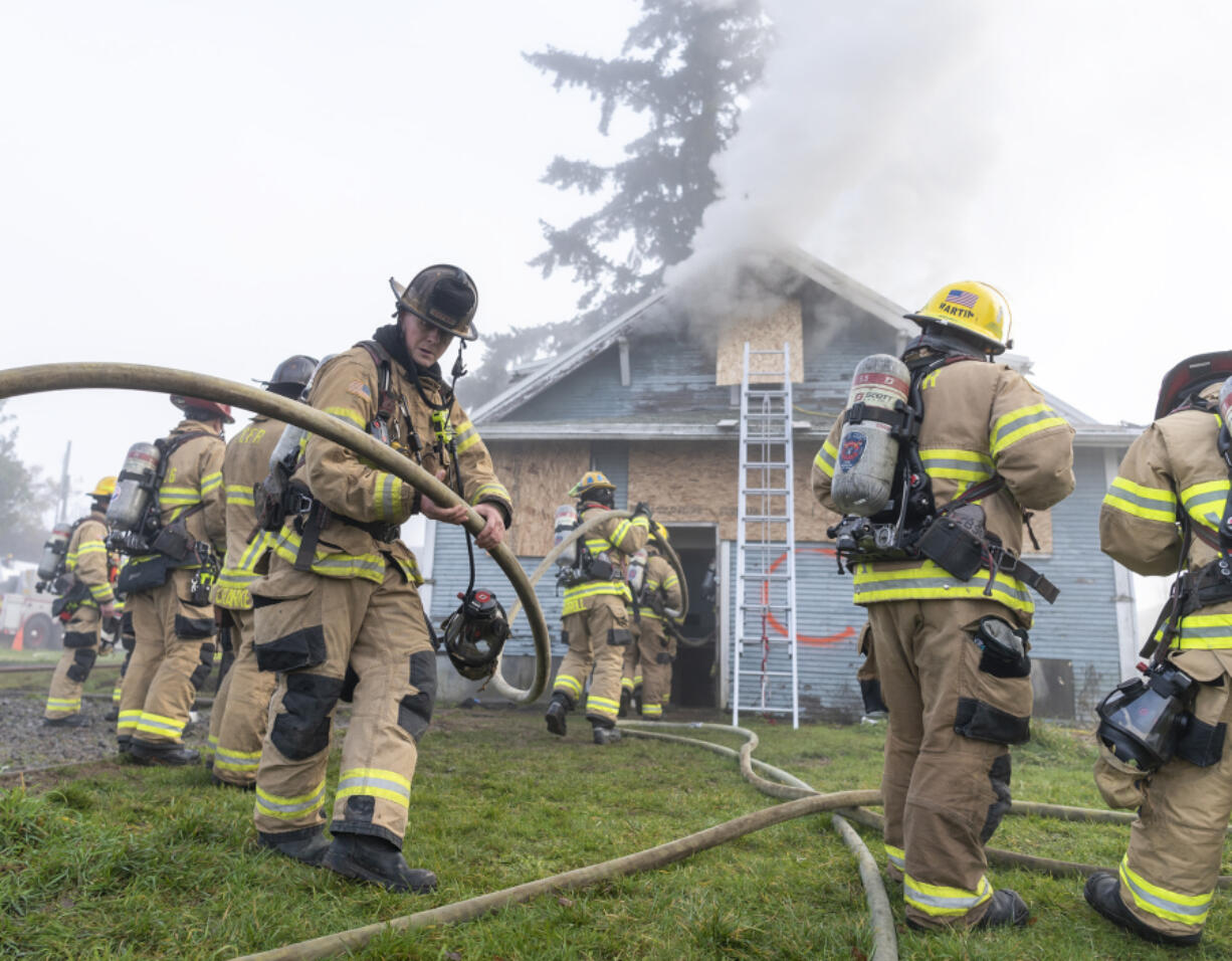 Firefighters carry a hose into a burning house Wednesday during a Clark-Cowlitz Fire Rescue training exercise in Ridgefield. For seven new firefighter/paramedics, the training marked their last exercise before graduating from the fire academy and joining the agency&rsquo;s ranks.