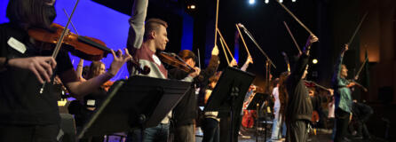 Vancouver School of Arts and Academics students conclude a practice performance with their bows in the air while joined by international recording artist and Emmy award-winning composer Mark Wood, right, in their school&rsquo;s auditorium Jan. 31. Wood is an original member of the multiplatinum selling Trans-Siberian Orchestra and creator of the revolutionary Viper electric violin. He visited VSAA with his groundbreaking music education program Electrify Your Strings!