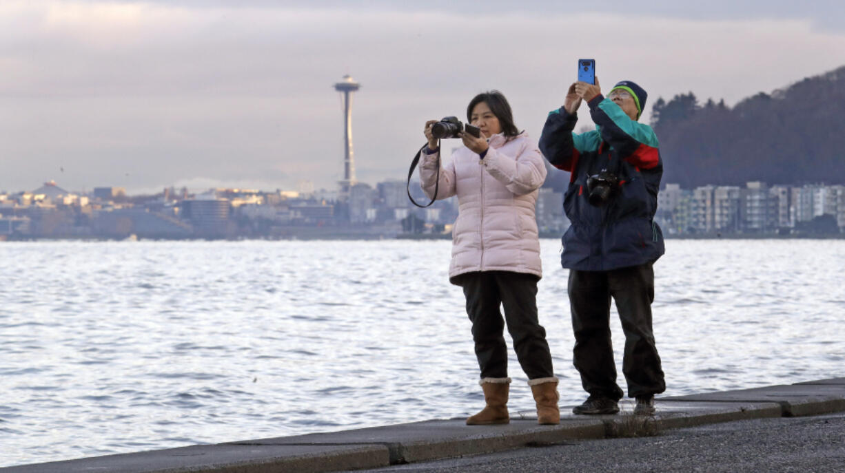 Anna Tsoi, left, and her husband, Tin Fuk, stand on a seawall and take photos of Puget Sound during an unusually high tide, often called a &ldquo;king tide,&rdquo; on Dec. 27, 2018, in Seattle.