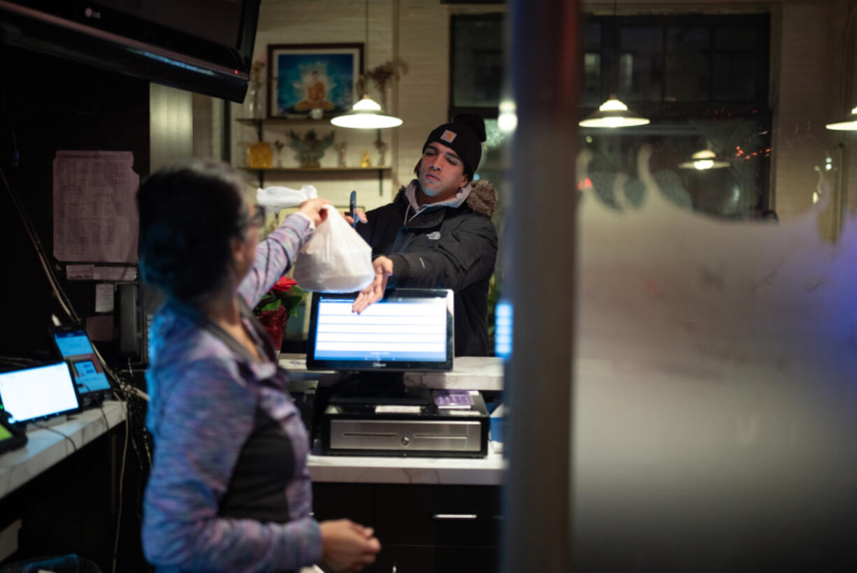 Sam Simonson hands a takeout order to a DoorDash delivery person at Sawatdee in Minneapolis on Thursday night, Dec. 14, 2023. Third party delivery food delivery services are a growing share of business at fast food restaurants and for other restaurants with cuisines that travel well, like the Thai menu at Sawatdee in Minneapolis, where they account for 30% of their business.