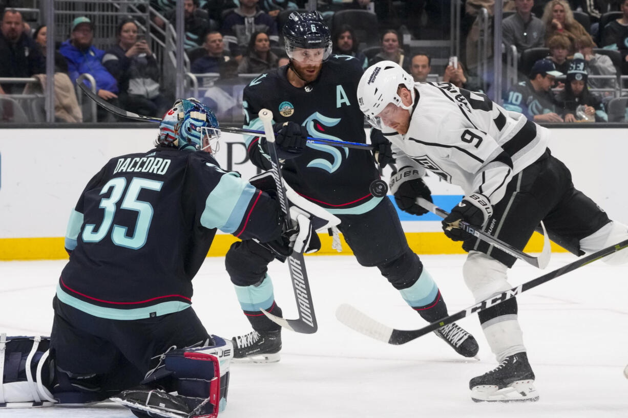 Los Angeles Kings right wing Carl Grundstrom (91) looks down at the puck as it flies up in front of him while trying to make a shot against Seattle Kraken goaltender Joey Daccord (35) and defenseman Adam Larsson (6) during the second period of an NHL hockey game Saturday, Dec. 16, 2023, in Seattle.