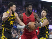 Portland Trail Blazers center Deandre Ayton, center, tries to turn toward the basket between Golden State Warriors guard Stephen Curry (30) and forward Trayce Jackson-Davis, right, during the first half of an NBA basketball game in San Francisco, Saturday, Dec. 23, 2023.