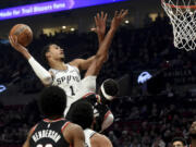 San Antonio Spurs center Victor Wembanyama, left, drives to the basket against Portland Trail Blazers center Moses Brown, center, as forward Jerami Grant, right, watches during the first half of an NBA basketball game in Portland, Ore., Thursday, Dec. 28, 2023.