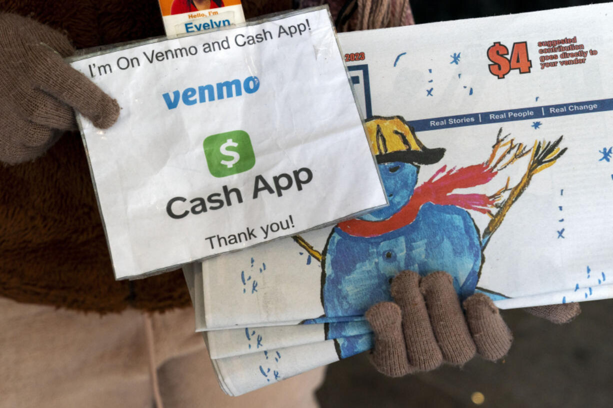 A vendor selling Street Sense, a local paper that covers issues related to the homeless and employs unhoused individuals as its vendors, holds up her sign saying she can accept donations from cashless apps like Venmo and CashApp, Wednesday, Dec. 6, 2023, in Washington. The transition to a cashless society has impacted street-level charitable giving &ndash; from individual donations to panhandlers to the Salvation Army donation kettles.