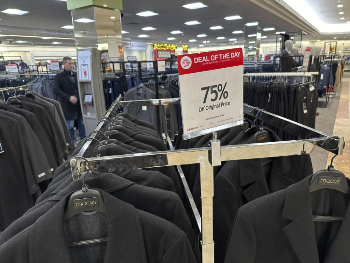 A shopper tries on a discounted coat in a Macy&rsquo;s department store on Friday, Dec. 15, 2023, in Denver. On Friday, the Commerce Department issues its November report on consumer spending. The report contains a measure of inflation that is closely watched by the Federal Reserve, which has recently paused hiking its key lending rate.