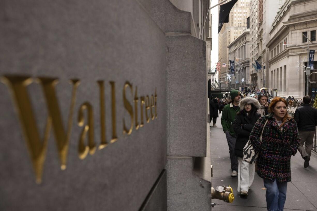 People walk past a Wall Street sign outside the New York Stock Exchange, Monday, Dec. 11, 2023, in New York. Wall Street is inching up modestly Wednesday ahead of a decision by the U.S.