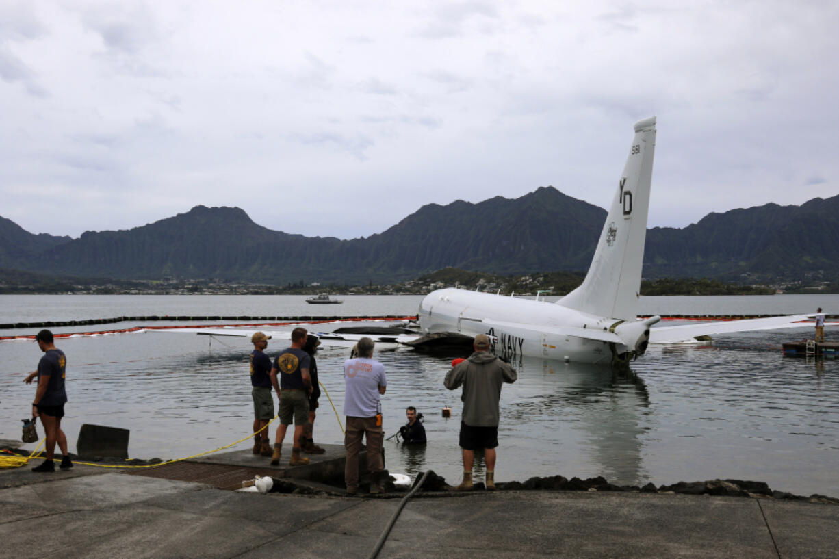 Contractors place inflatable bags under a U.S. Navy P-8A in Kaneohe Bay, Hawaii, Friday, Dec. 1, 2023, so they can float the aircraft over the water and onto land. The Navy plans to use inflatable cylinders to lift the jet off a coral reef and then roll it over to a runway to remove the plane from the ocean where it crashed the week before.