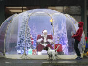 FILE - Santa Claus, portrayed by Dan Kemmis, laughs as he talks to Kristin Laidre as she walks her dog, Scooby, a Bassett Hound mix, as he sits inside a &ldquo;snow globe&rdquo; protective bubble due to the coronavirus pandemic in Seattle&rsquo;s Greenwood neighborhood on Dec. 8, 2020. (AP Photo/Ted S.