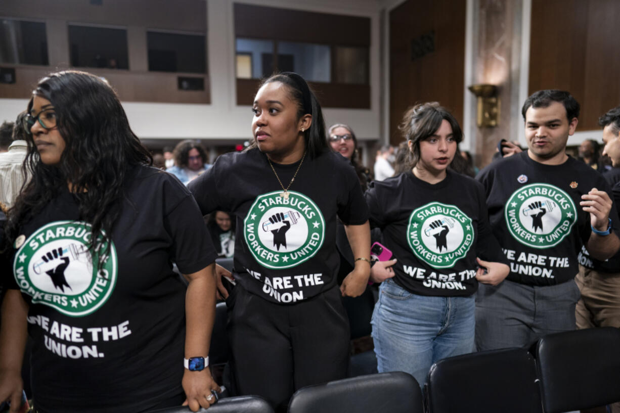 File - Advocates for a union for Starbucks employees watch as company founder Howard Schultz leaves a hearing after testifying to the Senate Health, Education, Labor and Pensions Committee at the Capitol in Washington on March 29, 2023. Starbucks says it&rsquo;s committed to bargaining with unionized workers and reaching labor agreements next year. The move Friday is major reversal for the coffee chain after two years fighting the unionization of its U.S. stores. (AP Photo/J.