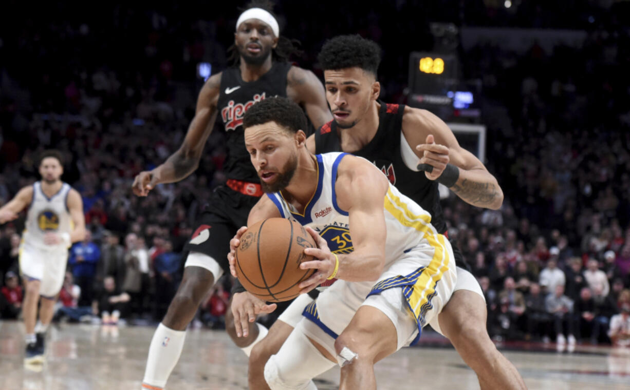 Golden State Warriors guard Stephen Curry, front, is defended by Portland Trail Blazers forward Toumani Camara, right, and forward Jerami Grant, left, in the closing seconds of the second half of an NBA basketball game in Portland, Ore., Sunday, Dec. 17, 2023.