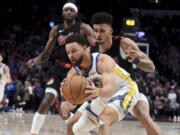 Golden State Warriors guard Stephen Curry, front, is defended by Portland Trail Blazers forward Toumani Camara, right, and forward Jerami Grant, left, in the closing seconds of the second half of an NBA basketball game in Portland, Ore., Sunday, Dec. 17, 2023.
