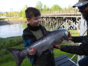 Nine-year-old Bradly Reed gets a hand from Nate Hall of The Bait Shack as he holds up a 17.45 pound king salmon he caught during an incoming tide at Ship Creek near downtown Anchorage, Alaska, on June 5, 2023.