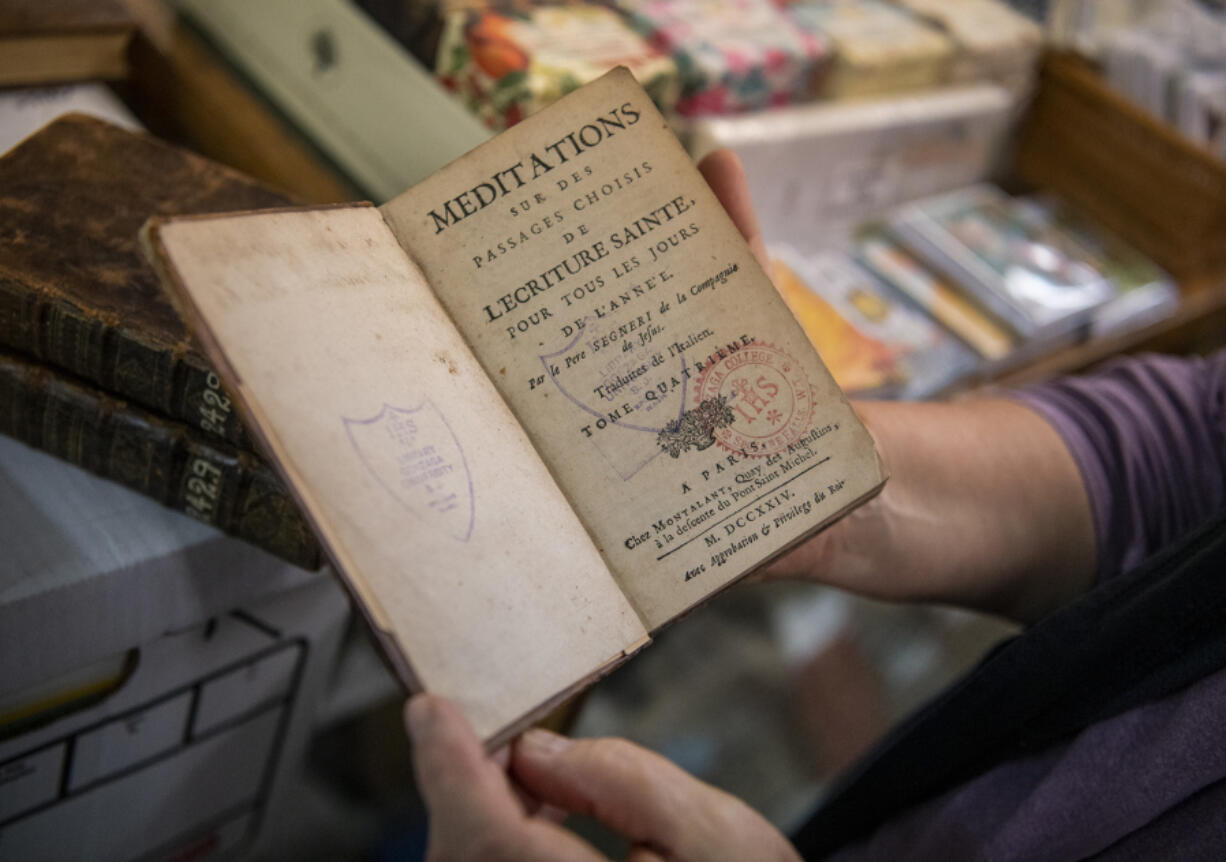 Pepper Parker, a 19-year employee of Vintage Books, holds a 1724 French book of scripture at Vintage Books in Vancouver.