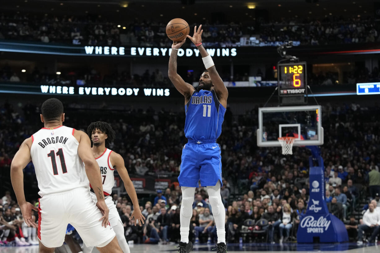 Dallas Mavericks guard Kyrie Irving, right, pulls up for a jump shot against Portland Trail Blazers defenders Malcolm Brogdon, left, and Shaedon Sharpe, center, during the first half of an NBA basketball game in Dallas, Friday, Jan. 5, 2024.