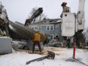 Jose Peralta, with the Oregon Department of Forestry, uses a chainsaw to cut a downed tree into smaller pieces after it fell on a car and a home on Saturday, Jan. 13, 2024, in Portland, Ore.