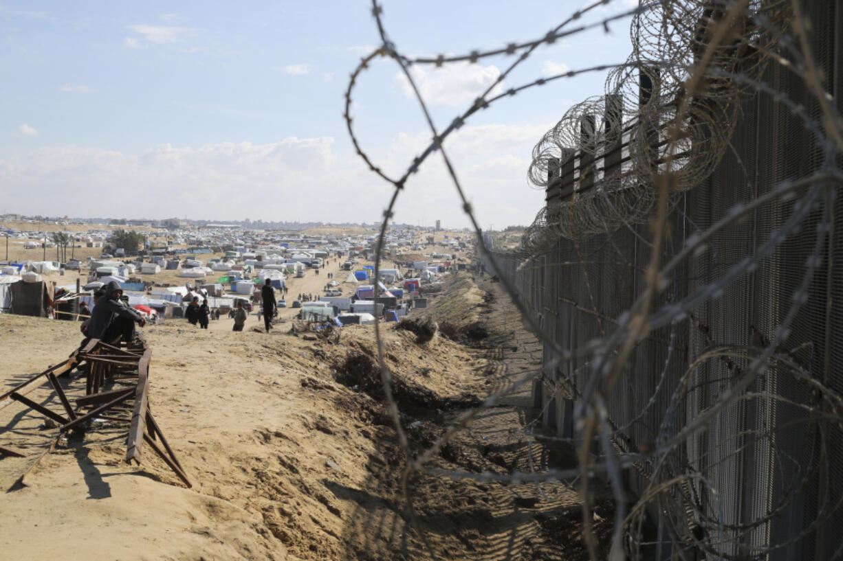 Palestinians displaced by the Israel air and ground offensive on the Gaza Strip sit next to the border fence with Egypt in Rafah, Wednesday, Jan. 24, 2024. Israel and Egypt are engaged in an increasingly public spat over a narrow strip of land between Egypt and Gaza. That strip is the Philadelpi Corridor. The dispute puts Israel in a bind. If it stops its military offensive against Hamas without taking control of the southern Gaza city Rafah on the border with Egypt, it falls short on its top war goal of crushing the Islamic militants. If its military pushes south to the border, it risks undermining its peace deal with Egypt and likely upsetting its closest ally, the United States. The Egypt-Israel peace deal has been a pillar of stability in a turbulent Middle East.