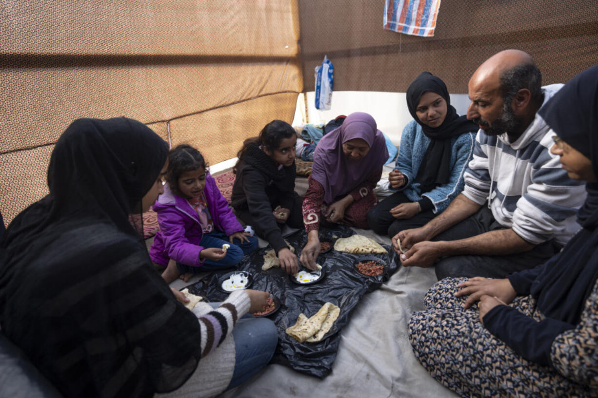 Members of the Abu Jarad family, who were displaced by the Israeli bombardment of the Gaza Strip, eat breakfast at a makeshift tent camp in the Muwasi area, southern Gaza, Monday, Jan. 1, 2024.