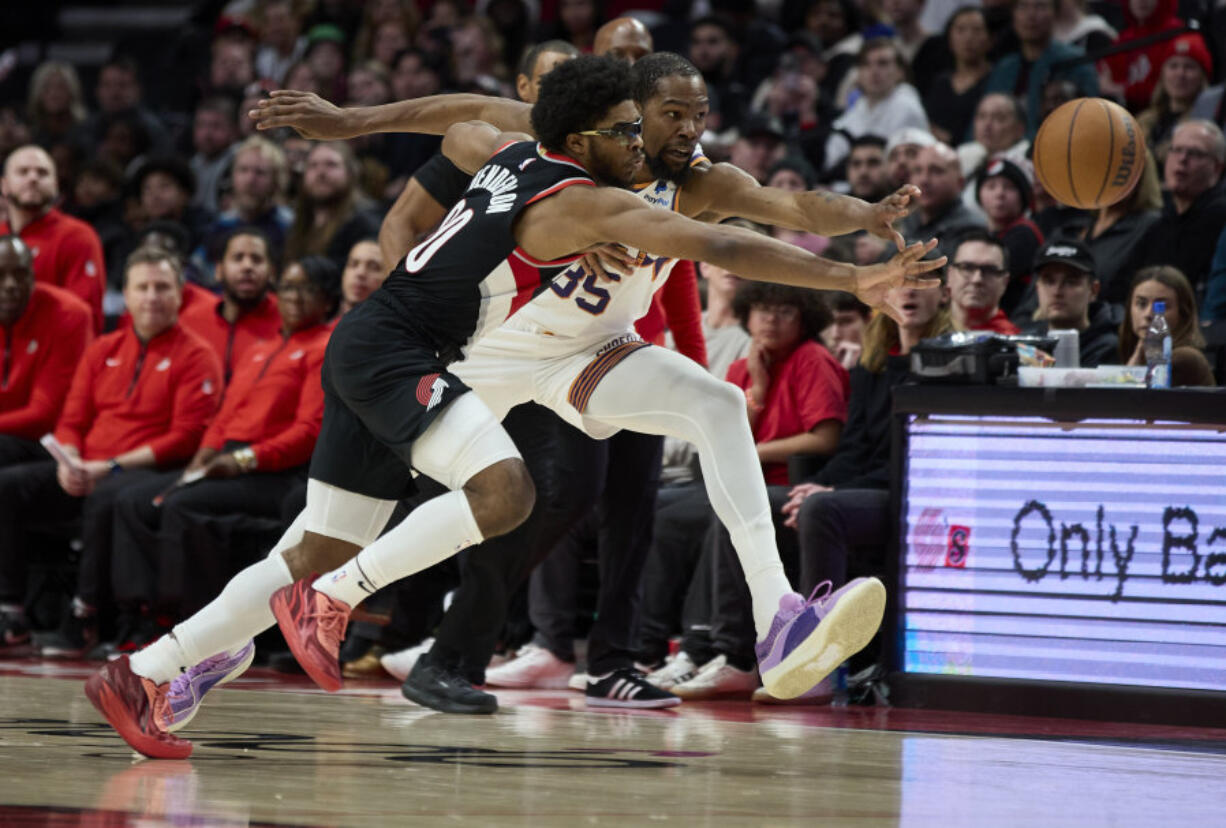 Portland Trail Blazers guard Scoot Henderson, left, and Phoenix Suns forward Kevin Durant, right, reach for thse ball during the second half of an NBA basketball game in Portland, Ore., Sunday, Jan. 14, 2024.