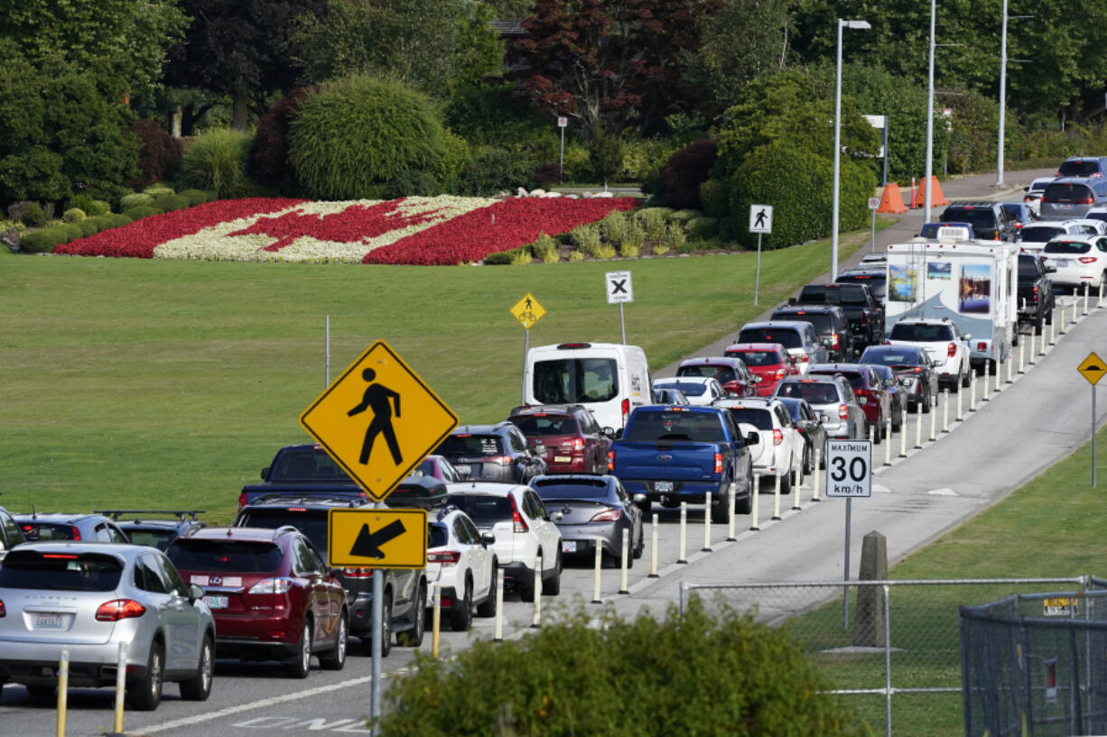 A line of vehicles wait to enter Canada at the Peace Arch border crossing in view of a Canadian flag made of flowers Aug. 9, 2021, in Blaine.