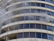 People in Smith Tower look out from a balcony, bottom left, as smoke billows out from a nearby window during a two-alarm fire downtown Friday morning, Feb. 23, 2024.