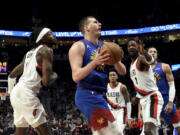 Denver Nuggets center Nikola Jokic, center, drives to the basket against Portland Trail Blazers forward Jerami Grant, left, and center Deandre Ayton, front right, during the first half of an NBA basketball game in Portland, Ore., Friday, Feb. 23, 2024.