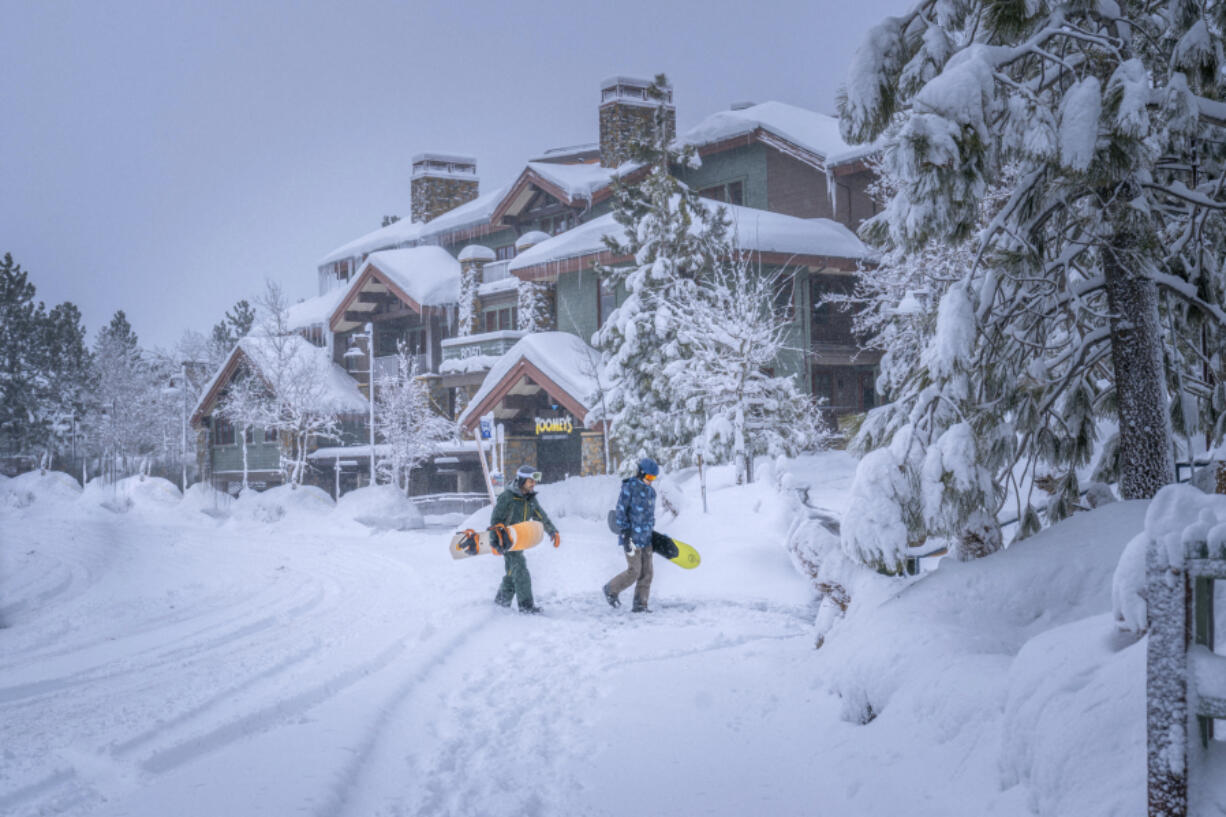 In this photo provided by Mammoth Lakes Tourism, snowboarders walk in the snow on Monday, Feb. 19, 2024, in Mammoth Lakes, Calif.