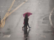 People cross the street with umbrellas in heavy rain in Los Angeles, Monday, Feb. 19, 2024.