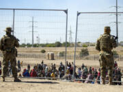 FILE - Migrants wait in line adjacent to the border fence under the watch of the Texas National Guard to enter into El Paso, Texas, May 10, 2023. Senators are racing to release a highly-anticipated bill that pairs border enforcement policy with wartime aid for Ukraine, Israel and other U.S. allies, as part of a long-shot effort to push the package through heavy skepticism from Republicans, including House Speaker Mike Johnson.