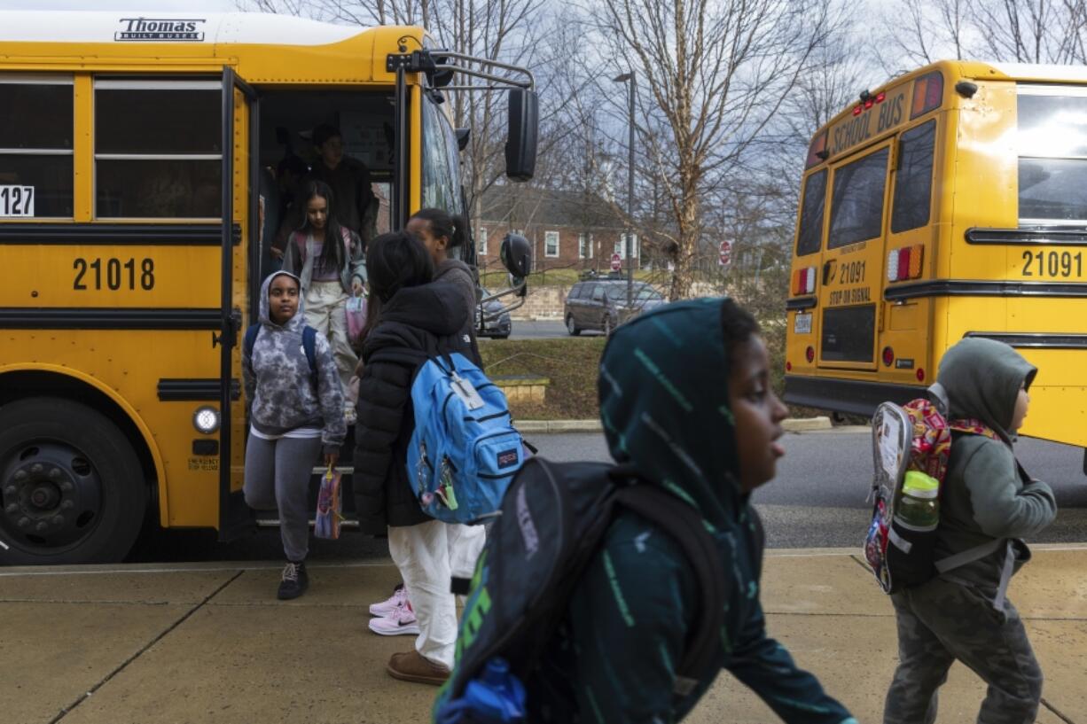 Rock Creek Forest Elementary School students exit a diesel bus before attending school, Friday, Feb. 2, 2024, in Chevy Chase, Md. At right is an electric school bus.