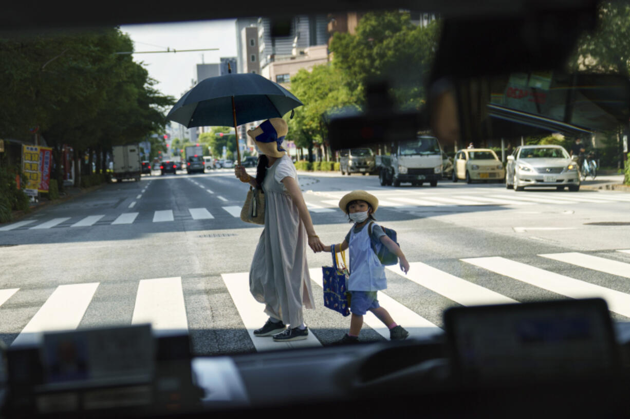 FILE - A pedestrian crossing a street with a child is seen through a taxi window in Tokyo, Monday, July 19, 2021.  The number of babies born in Japan last year fell for an eighth straight year to a new low, government data showed Tuesday, Feb. 27, 2024, and a top official said it was critical for the country to reverse the trend in the coming half-dozen years.