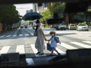 FILE - A pedestrian crossing a street with a child is seen through a taxi window in Tokyo, Monday, July 19, 2021.  The number of babies born in Japan last year fell for an eighth straight year to a new low, government data showed Tuesday, Feb. 27, 2024, and a top official said it was critical for the country to reverse the trend in the coming half-dozen years.